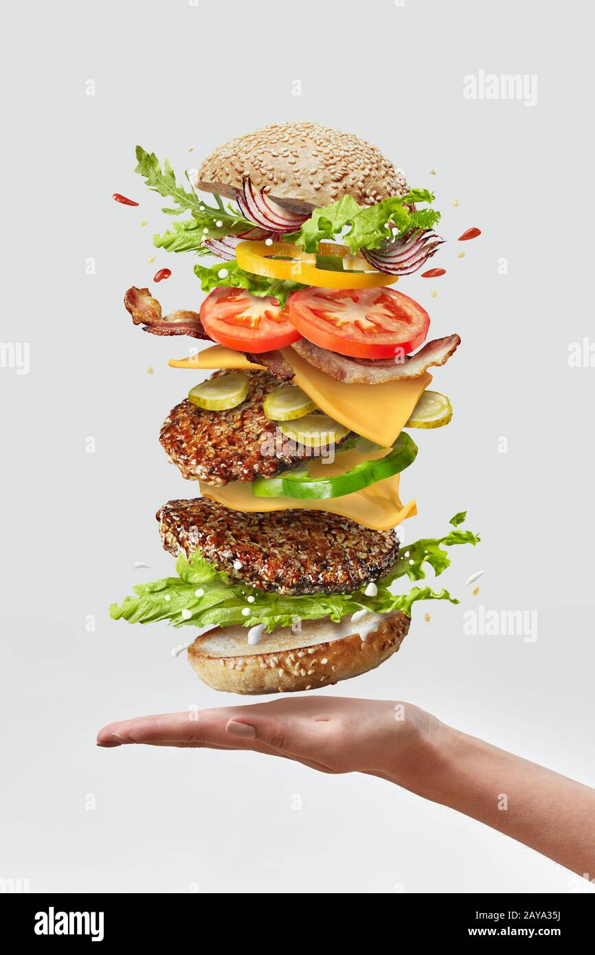 Köstliche hausgemachte Burger auf eine Frau hand mit fliegenden frische Zutaten auf einem weißen Hintergrund. Kopieren Sie Platz. Stockfoto