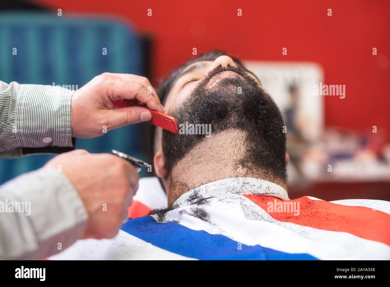Barber rasiert den Bart eines gutaussehenden bärtigen Mannes mit einem elektrischen Rasierer im barber Shop. Stockfoto