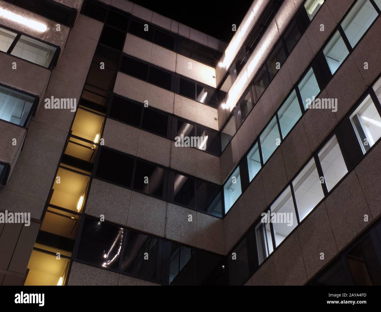 Die Ecke eines Bürogebäudes in der Nacht mit beleuchteten Wänden und Lichtern, die auf der Außenseite leuchten Stockfoto
