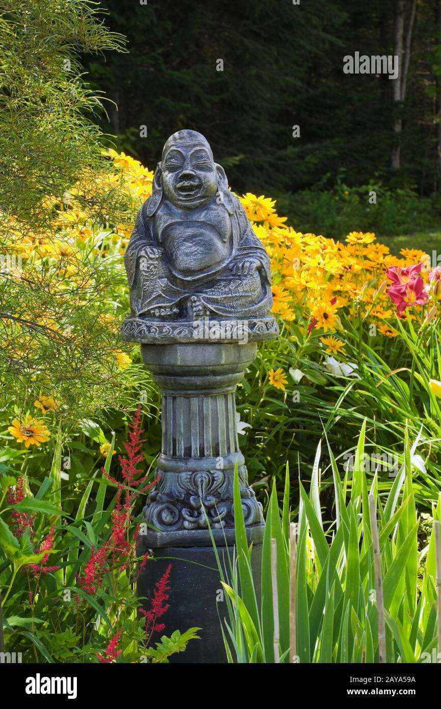 Zementstatue des Buddha auf einer Säule in der Grenze zu rotem Astylbe 'Radius' und gelbem Rudbeckia - Coneflowers im Garten Des Hinterhofes Im Sommer Stockfoto
