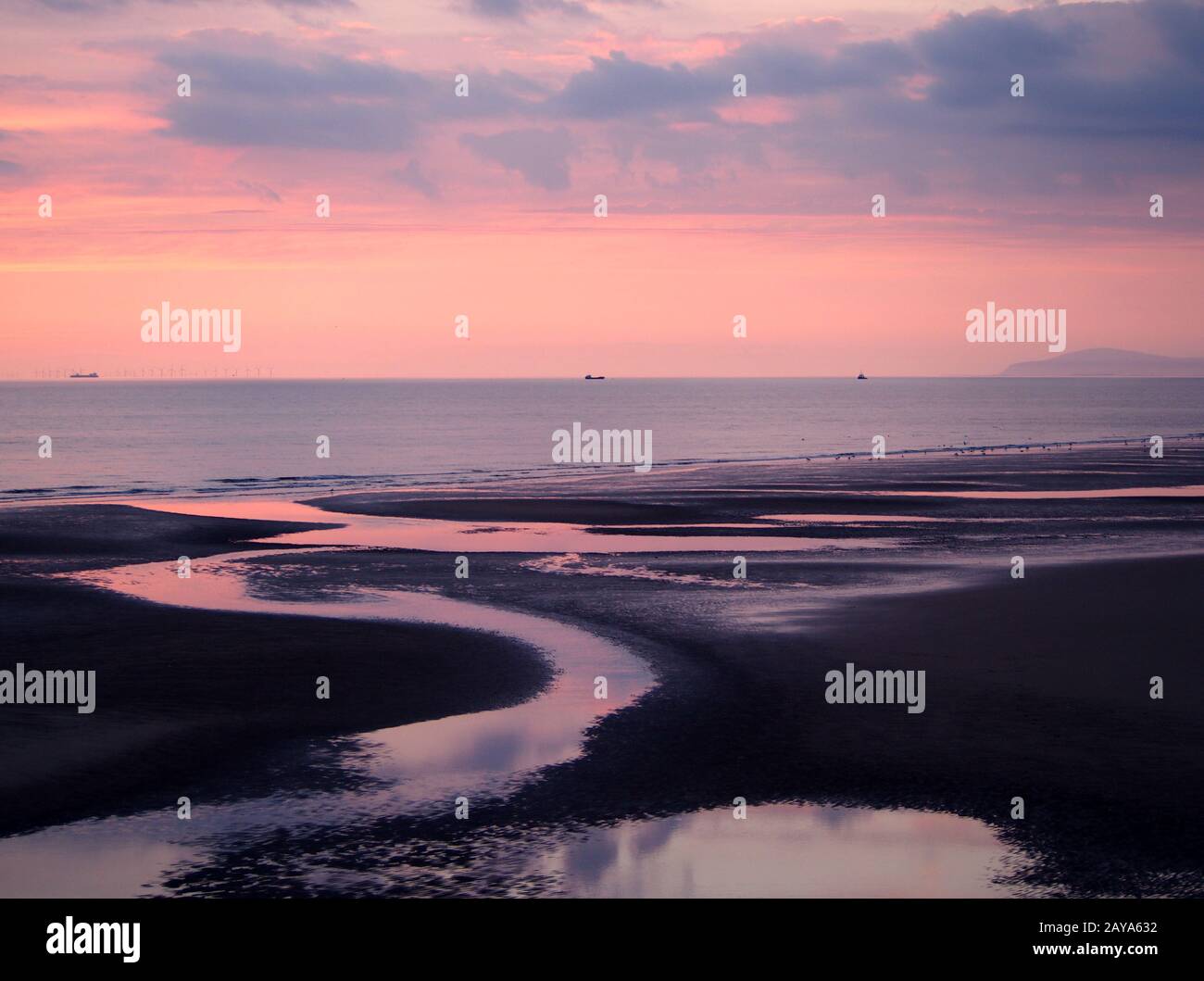 Dunkler Strand mit rosafarbenem Himmel nach Sonnenuntergang mit blauen Wolken, die bei Ebbe im Wasser reflektiert werden Stockfoto