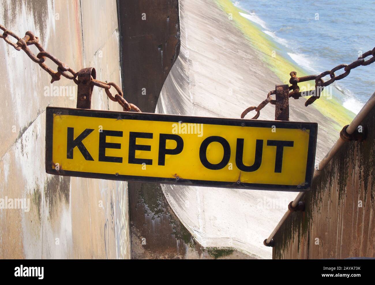 Gelbes Schild "Keep Out" hing an einer Kette, die den Eingang zur Betonmeerwand blockierte, die bei Flut zum Strand führte Stockfoto
