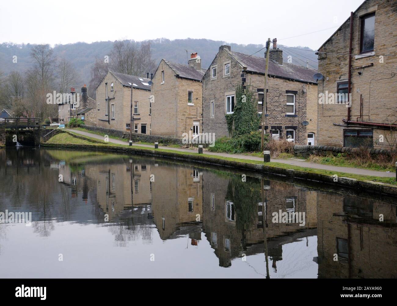 Häuser neben der Rochdale Canal in Hebden Bridge mit Reflexionen im Wasser und Schleusentore in der Ferne Stockfoto