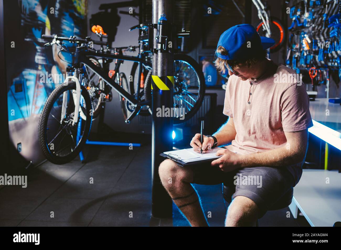 Der junge, gutaussehende, stylische Mann in einem Kappenschnapback und mit einem tattoo Kleinunternehmerbesitzer, der ein Fahrrad verkauft, sitzt die Werkstatt auf dem Stockfoto