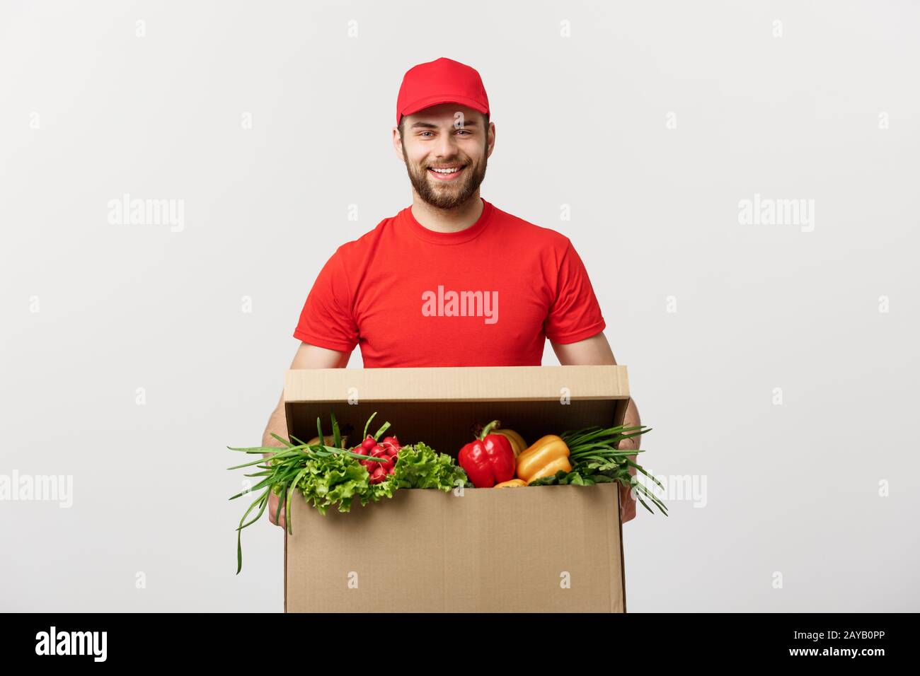 Lieferung Konzept: Stattlichen kaukasischen Lebensmittel-lieferservice Kurier Mann in der roten Uniform mit Lebensmittelgeschäft, mit frischem Obst und Gemüse Stockfoto