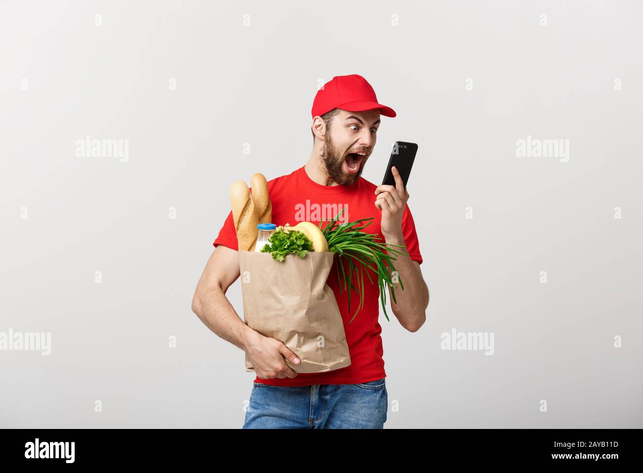 Lieferung Konzept: Stattlichen kaukasischen Lebensmittel-lieferservice Kurier Mann in der roten Uniform mit Lebensmittelgeschäft, mit frischem Obst und Gemüse Stockfoto