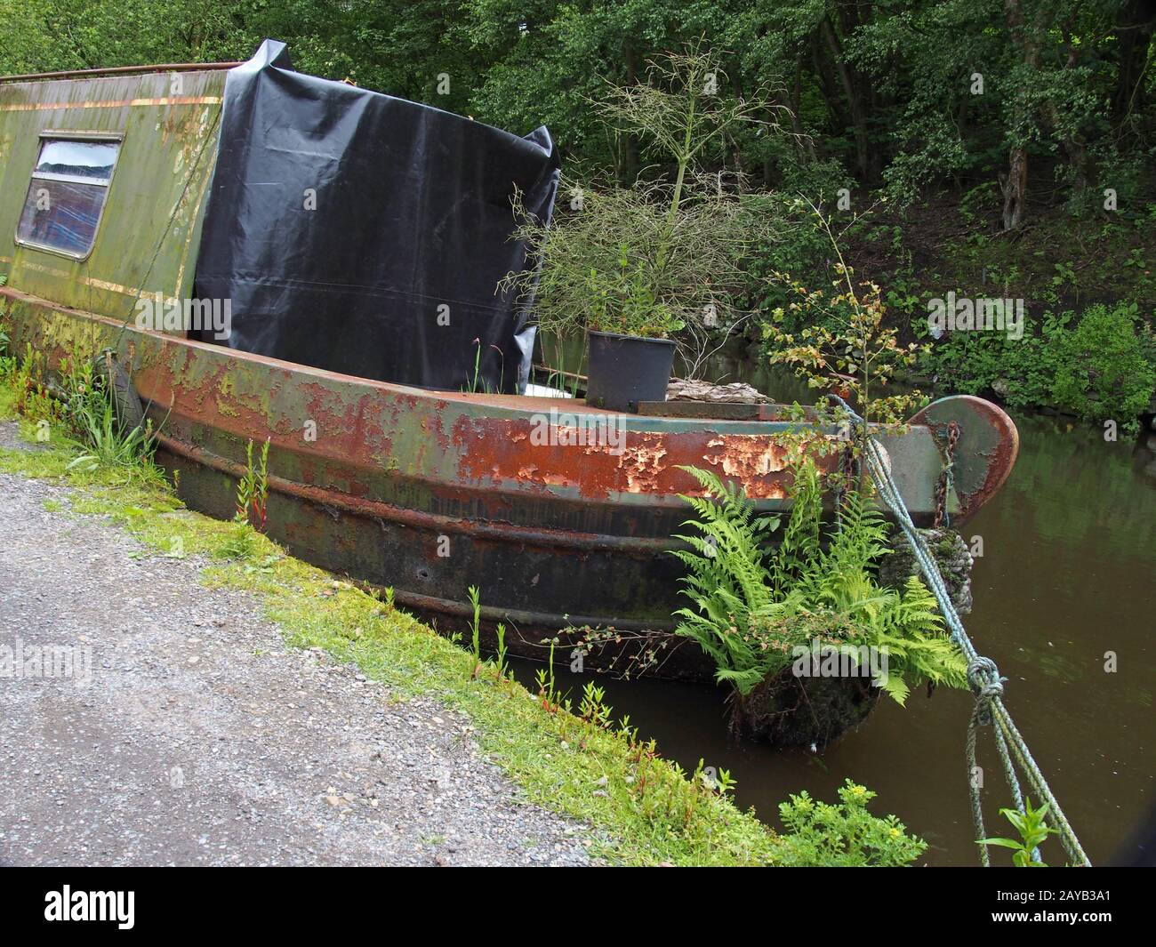 Ein altes rostendes Hausboot, das mit Unkraut überwuchert ist, das auf dem rochdale Kanal auf einer Seite verzeichnet ist und zu sinken beginnt Stockfoto