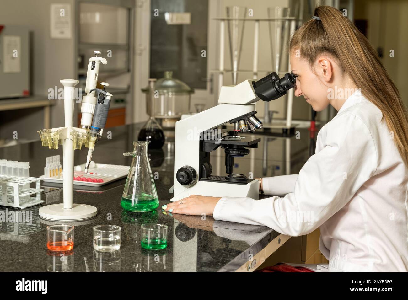 Junge Labortechnikerin, die am Mischmikroskop arbeitet Stockfoto