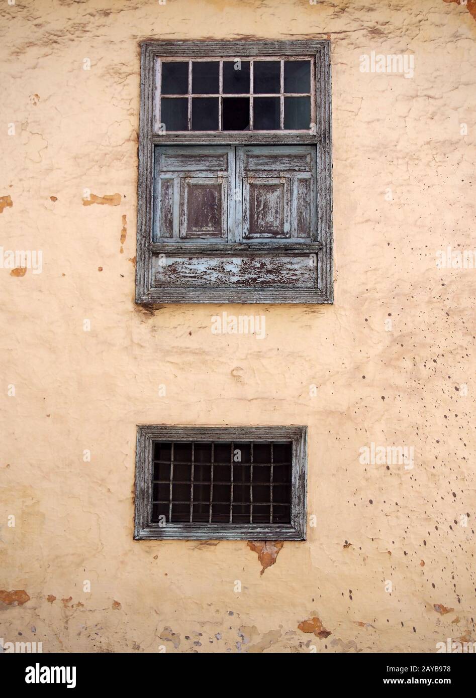 Zwei alte Holzfenster mit alten verblichenen grünen Farbbalken aus Metall blenden und Platten auf einer alten verputzten Schälbetonierung Stockfoto