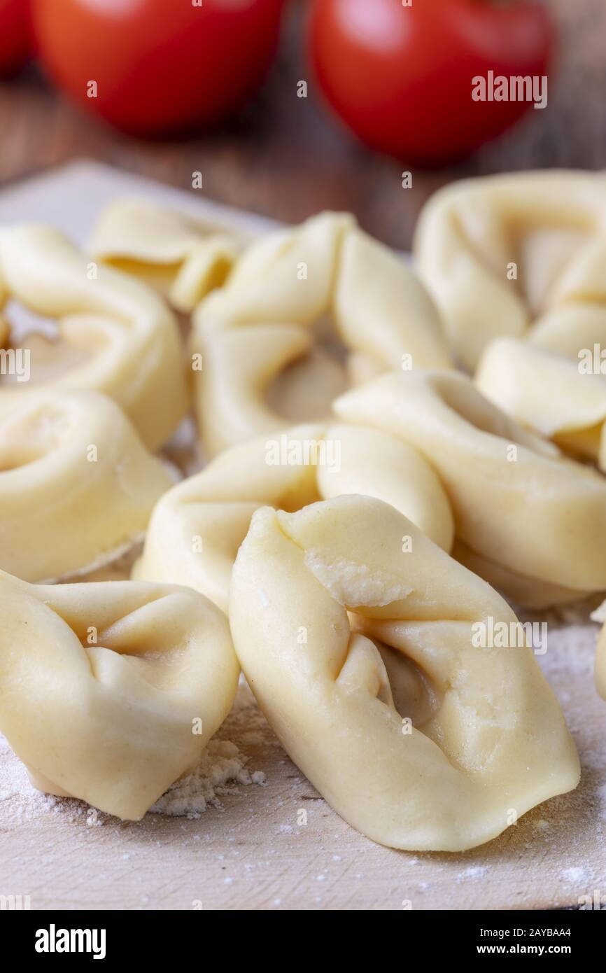 Roher Tortellini auf Holz mit Tomaten Stockfoto