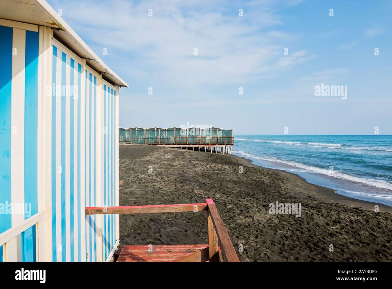 Das schöne Meer, der schwarze Sandstrand und weiß und blau gestreiften Beach Houses Stockfoto