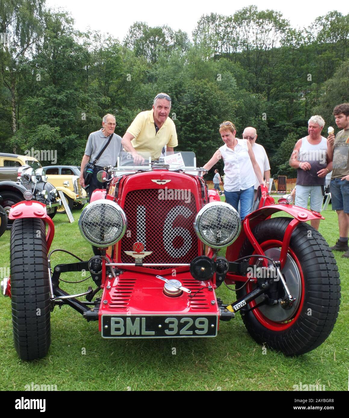 Ein Mann, der in einen alten sportwagen von aston martin kommt, mit Leuten, die im Park an der hebden Bridge das jährliche Vintage-Wochenende beobachten Stockfoto