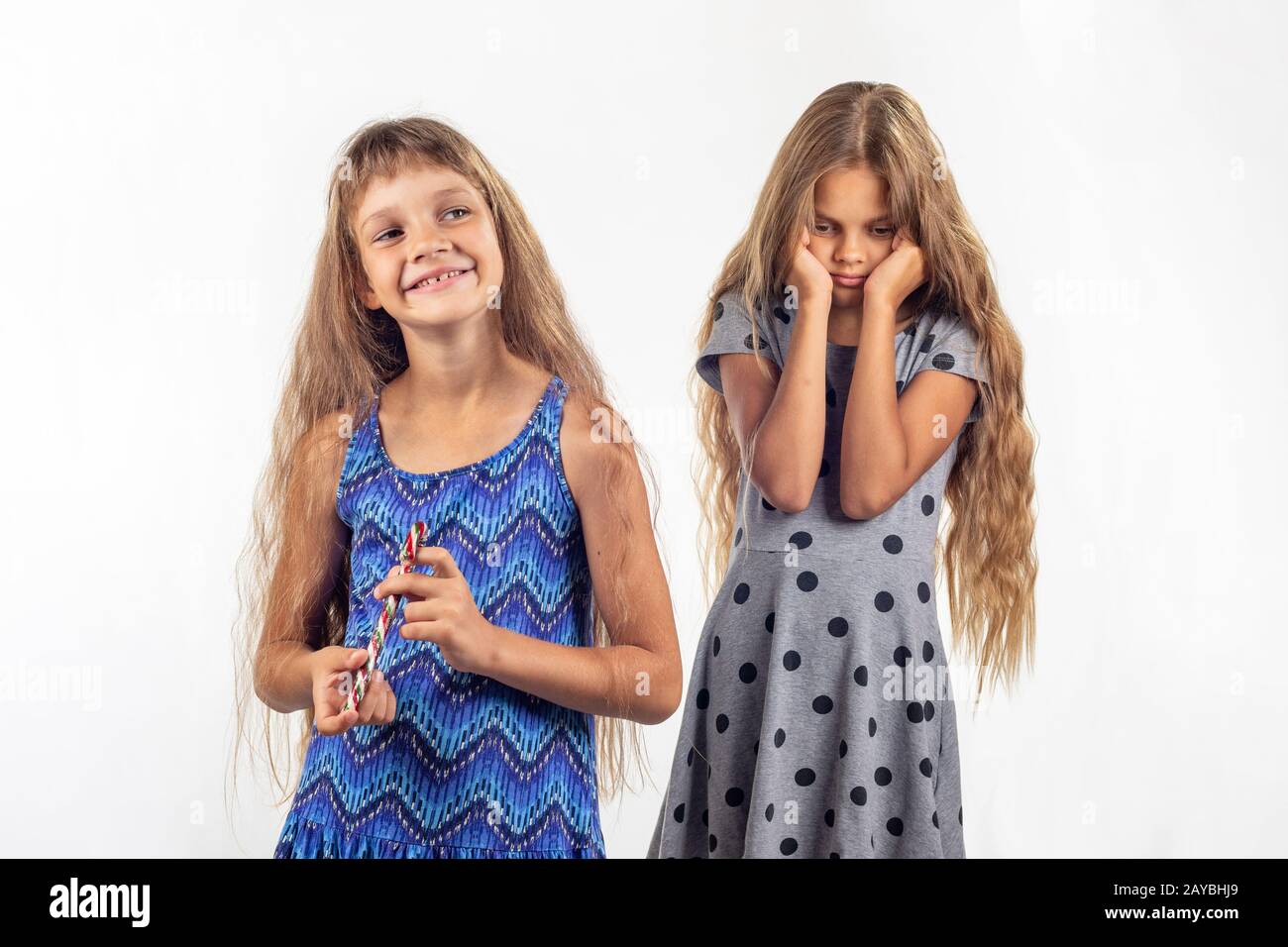 Mädchen hält freudig Süßigkeit, traurig, andere Mädchen im Hintergrund Stockfoto