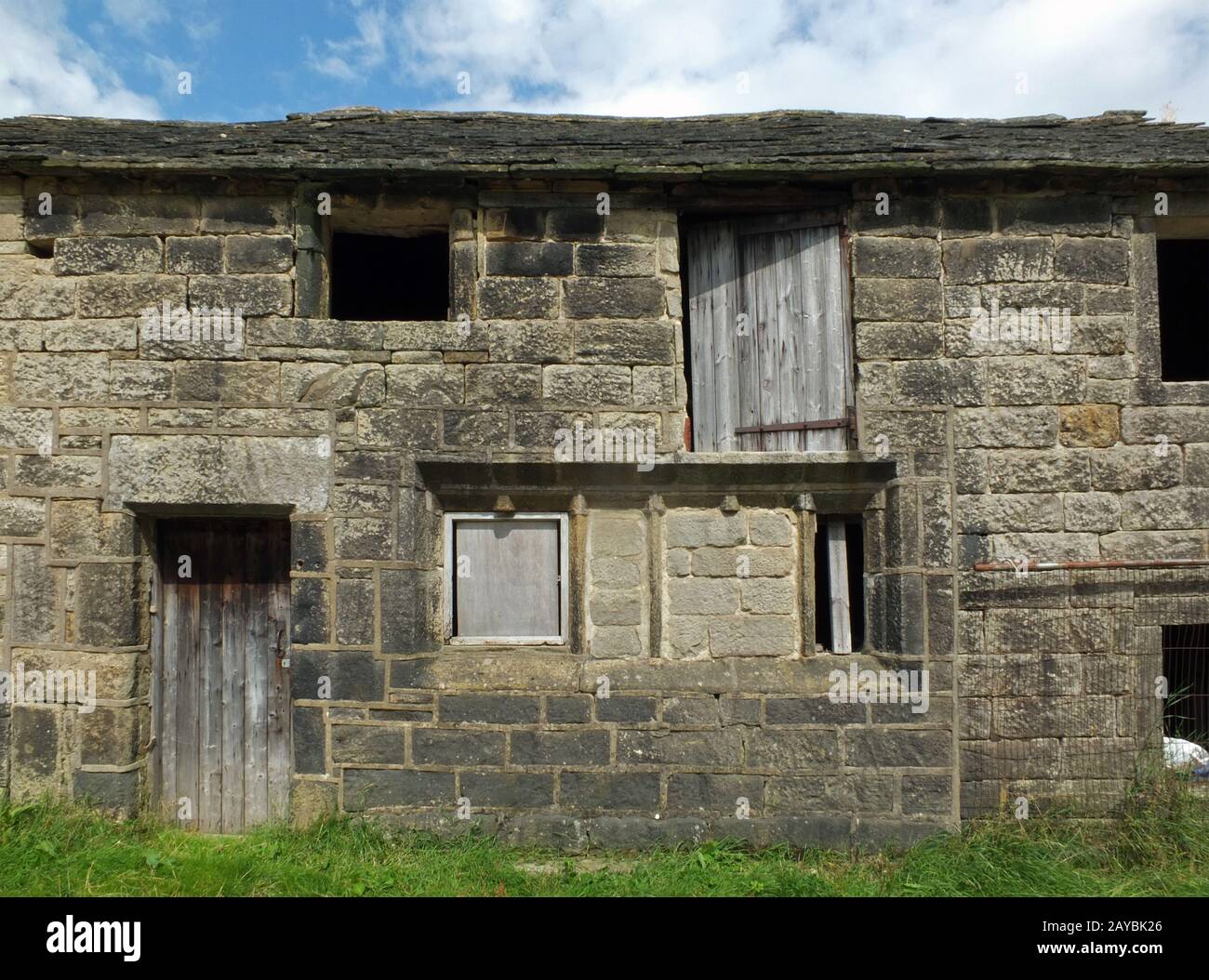 Altes vergangenes Steinhäuschen in einer Reihe ländlicher Gebäude mit leeren Fenstern und Holztüren mit dem Straßenbelag überwuchert Stockfoto
