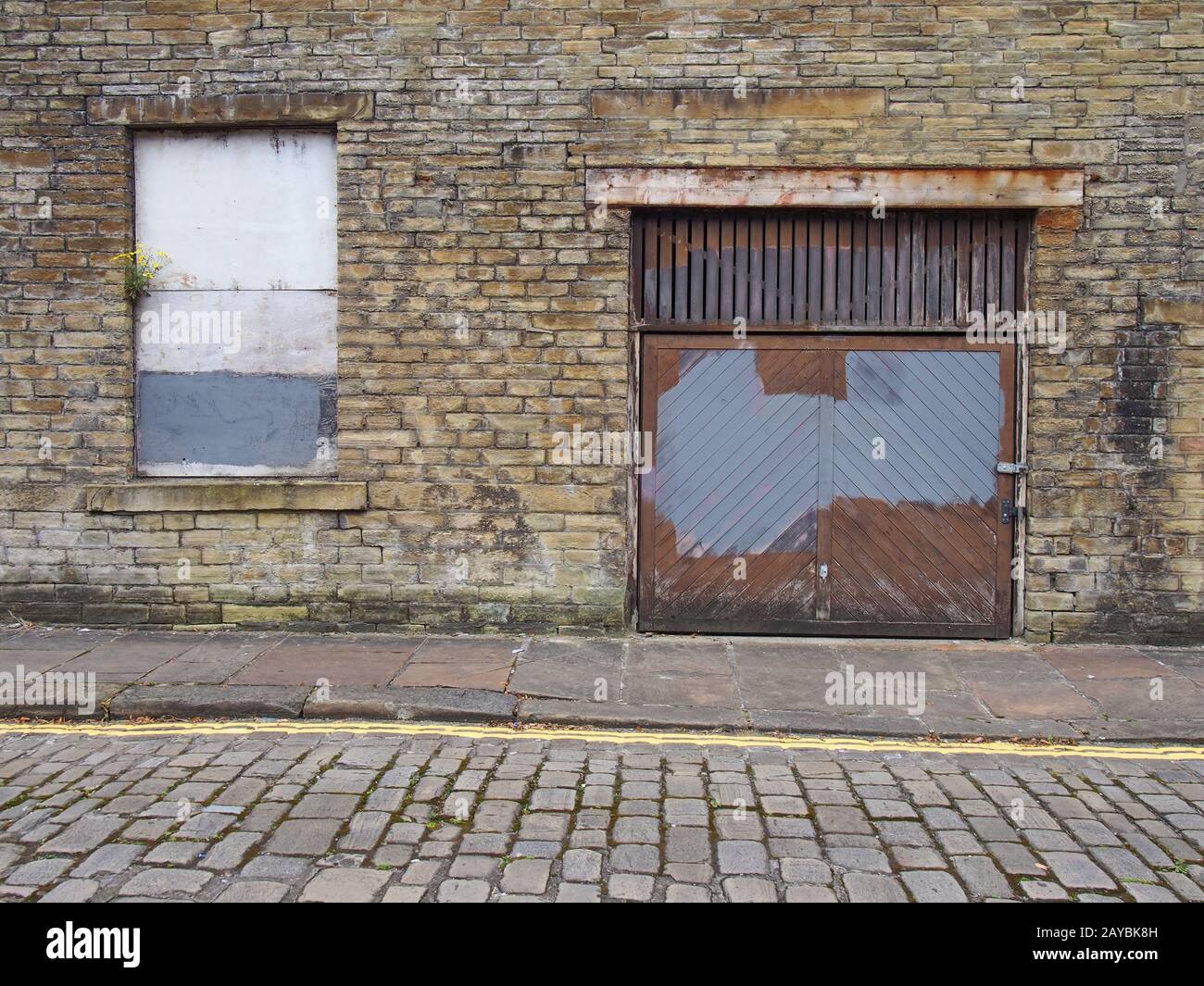 Vorderansicht eines alten verlassenen Gewerbegrundstücks auf einer leeren Straße mit Fenster und verfallener Ziegelmauer Stockfoto