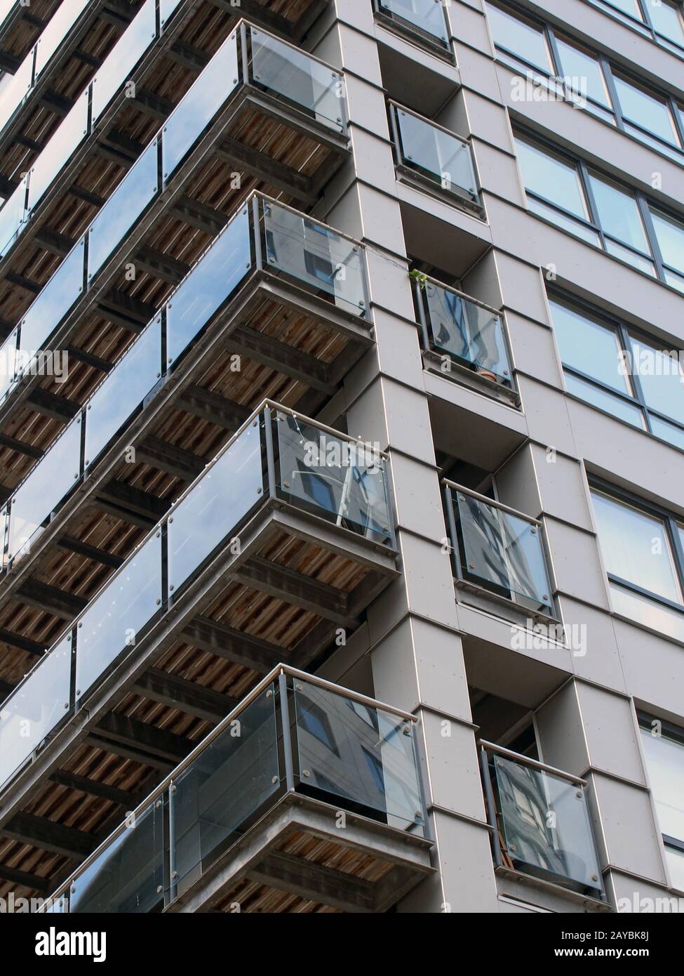 Eckansicht eines modernen städtischen Apartmentgebäudes mit schwarzer Verkleidung und gläsernen Balkonen, die andere Gebäude widerspiegeln Stockfoto