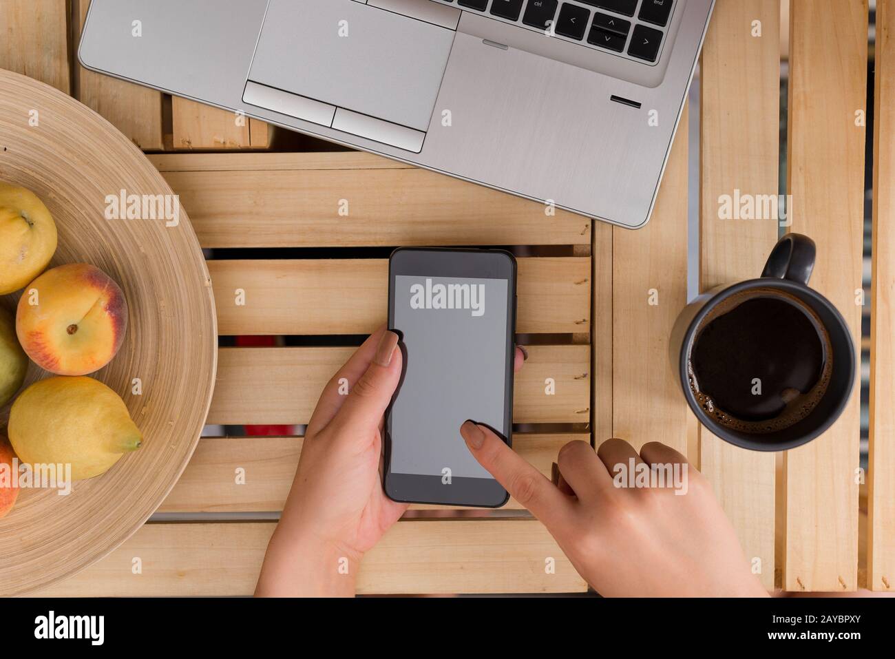 Junge Dame, die ein dunkles Smartphone in einem Kiste Tisch mit einem Becher schwarzen Kaffees benutzt und hält. Bürobedarf, Handy, Technol Stockfoto