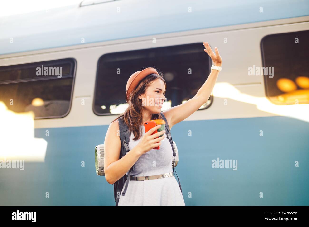Rucksackreisender Frau schwenkt Hand auf Bahnsteig Sommerurlaub Reisekonzept. Weibliche Touristenbegrüßung und enjo Stockfoto