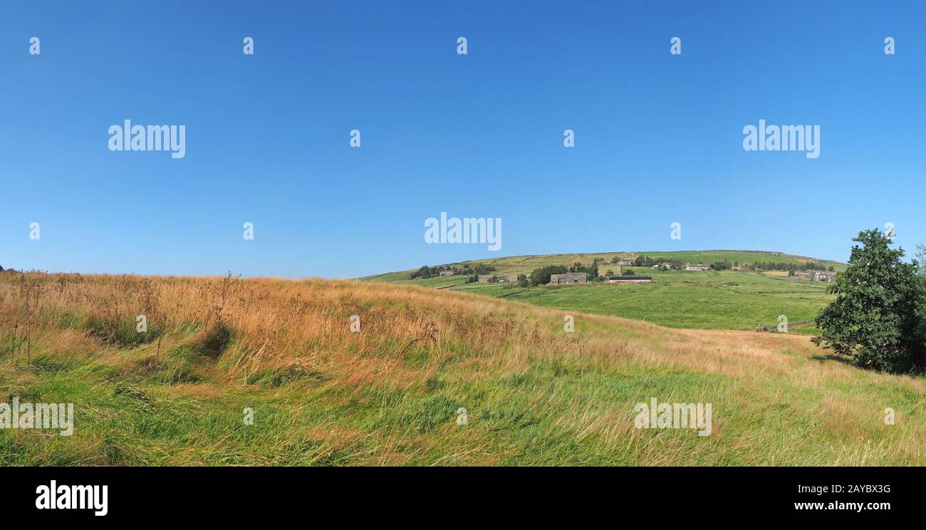 Lange Panoramasicht auf grüne Felder und entfernte Dorfsteinhäuser in der rollenden Landschaft der West yorkshire Dales in Colden mit Stockfoto