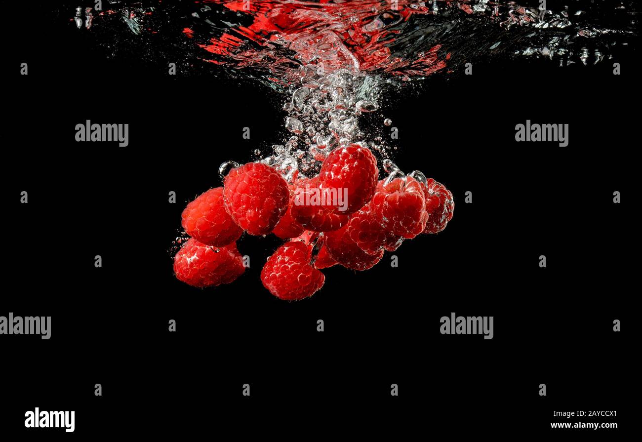 Roten Himbeeren fällt unter Wasser mit einem Spritzer, auf schwarzem Hintergrund isoliert. Stockfoto
