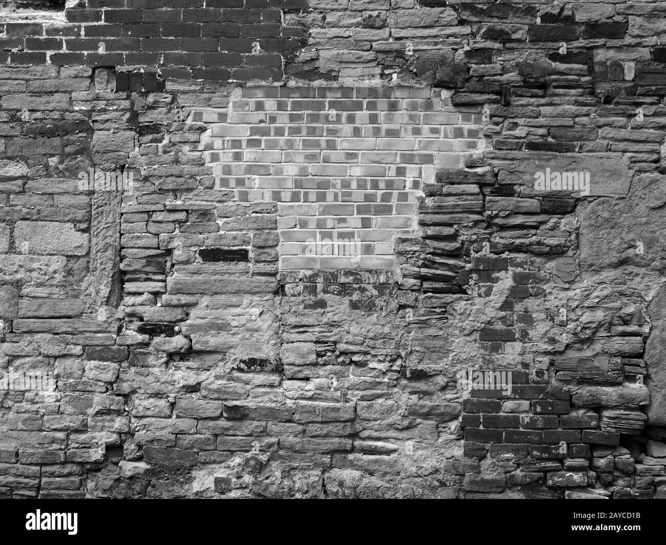 Monochrome reparierte und gepatchte Wand aus gemischten Backsteinen und Steinen Stockfoto