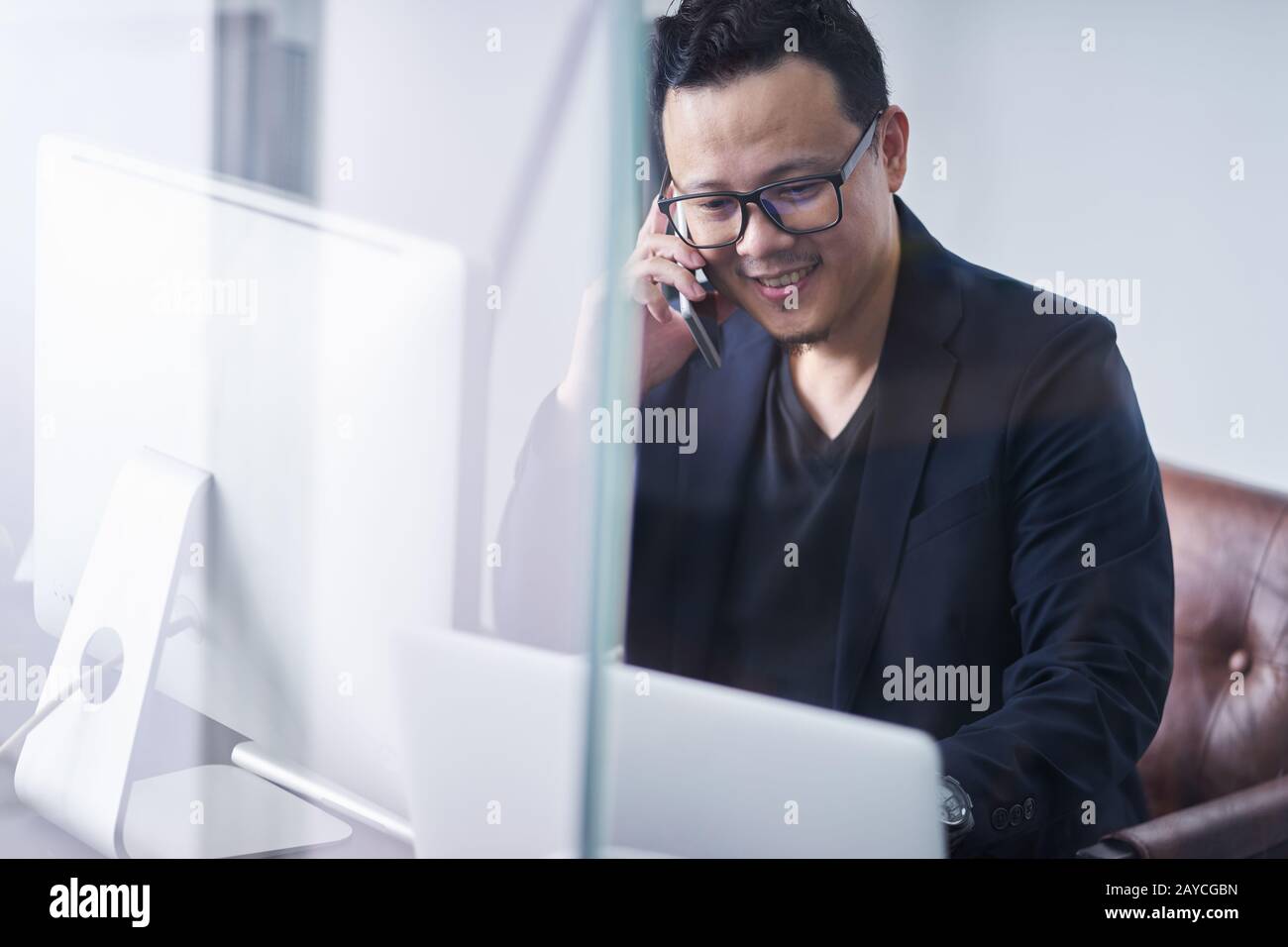 Junger asiatischer Geschäftsmann, der Handtelefon und Computer verwendet, arbeitet Stockfoto