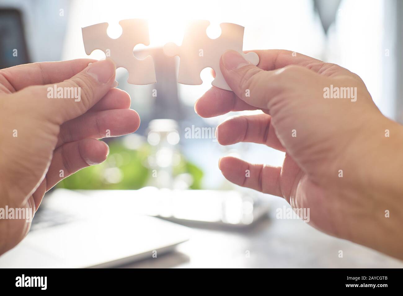 Junger Geschäftsmann, der versucht, ein Puzzleteil mit Sonnenschein und verwischtem Hintergrund zu verbinden Stockfoto