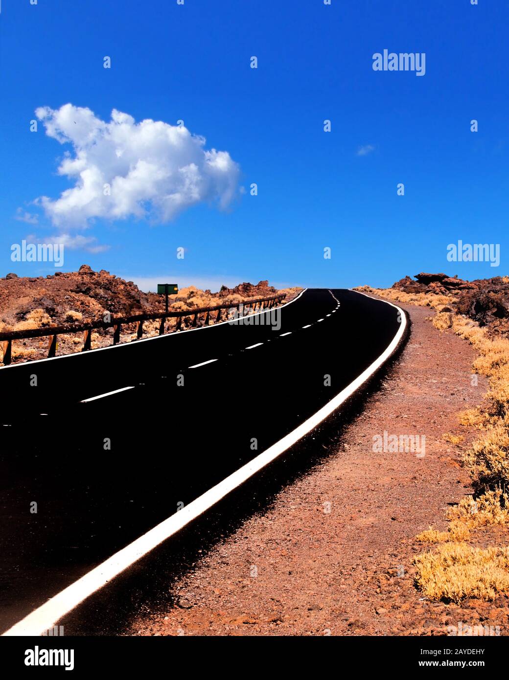 Eine zweispurige, leere Straße, die sich in einer zerklüfteten Wüstenlandschaft mit blauem bewölktem Himmel zum Horizont erstreckt Stockfoto