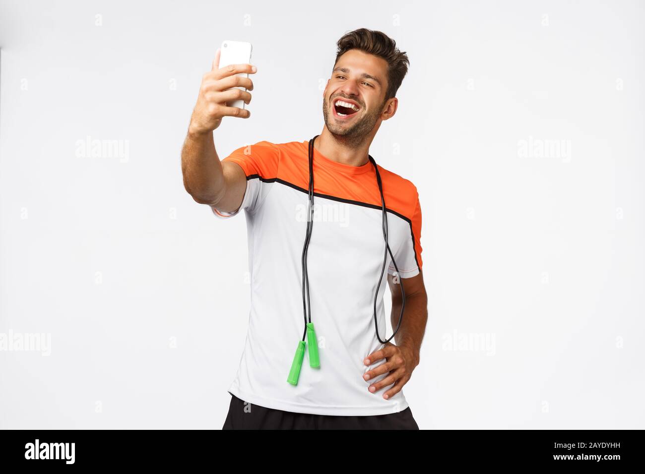 Gutaussehende, männliche Athletin nimmt selfie nach dem Training im Fitnessstudio, hält Smartphone mit verlängertem Arm, lächelt zufrieden und stolz, erzählt Stockfoto