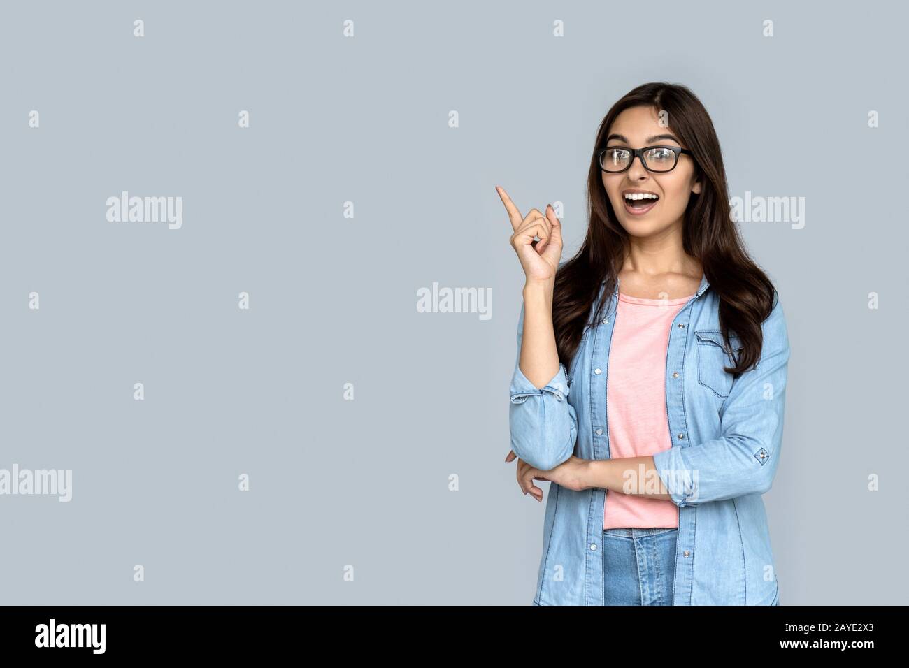 Verblüfftes indisches Mädchen, das mit dem Finger auf den Kopierraum zeigt, der auf grauem Hintergrund isoliert ist Stockfoto