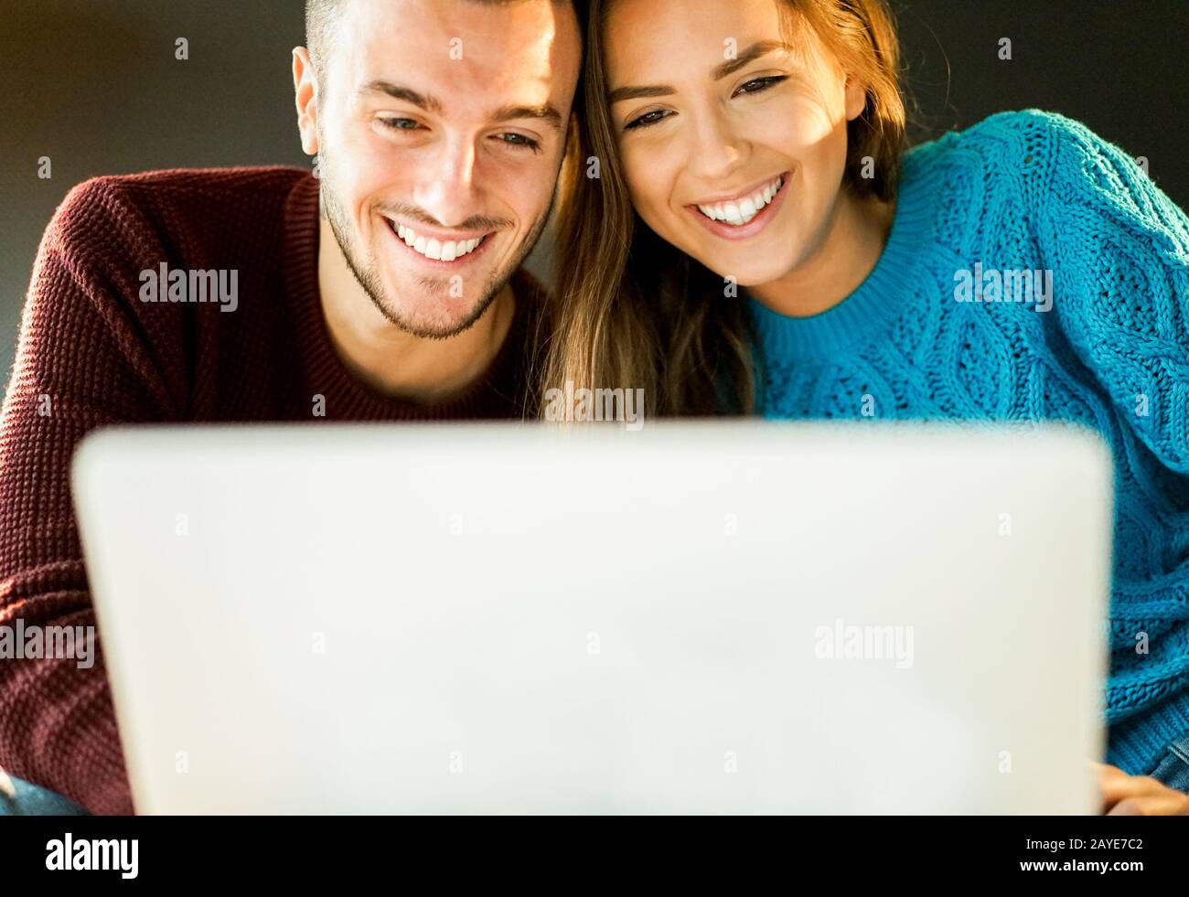 Gutaussehende glückliche Paare, die online einkaufen, mit einem Laptop - Jugendliche, die im Internet auf dem Sofa zu Hause surfen - Konsumfreuden und Beziehung Stockfoto