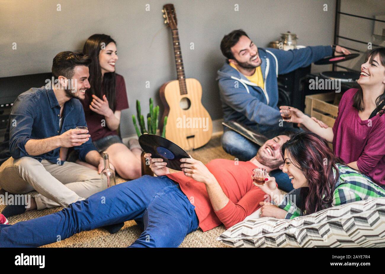 Fröhliche Freunde, die auf Vinyl-Alben im Hostelzimmer Party hören - Jugendliche, die Spaß haben, Schüsse zu trinken und gemeinsam zu lachen - Soft fo Stockfoto