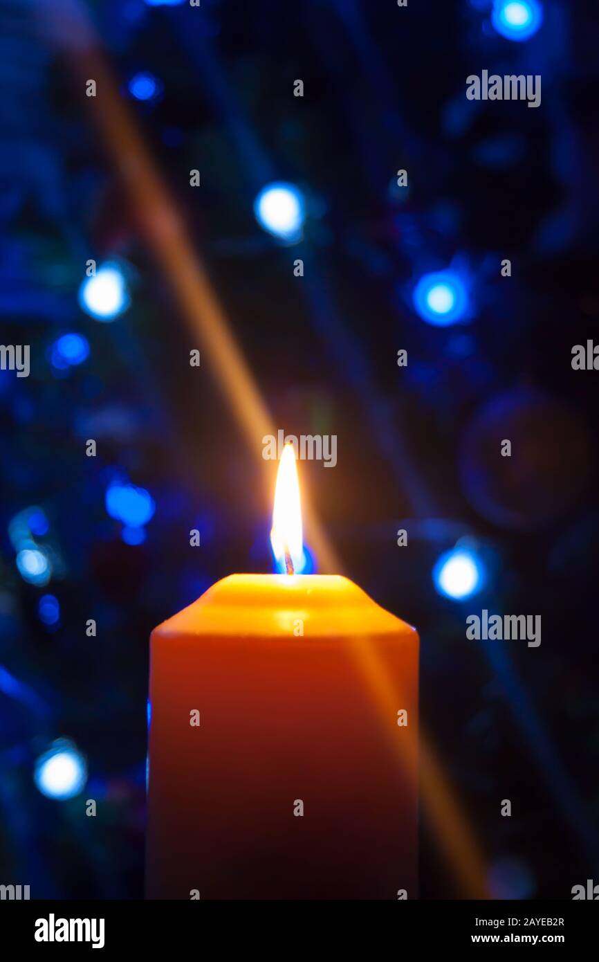 Eine große Kerze brennt vor dem Hintergrund einer Girlande mit strahlendem Licht. Vertikales Foto, Unschärfe. Mystische esoterische Romantik Divination Stimmung getauft Weihnachts-Karol-Setcer Stockfoto