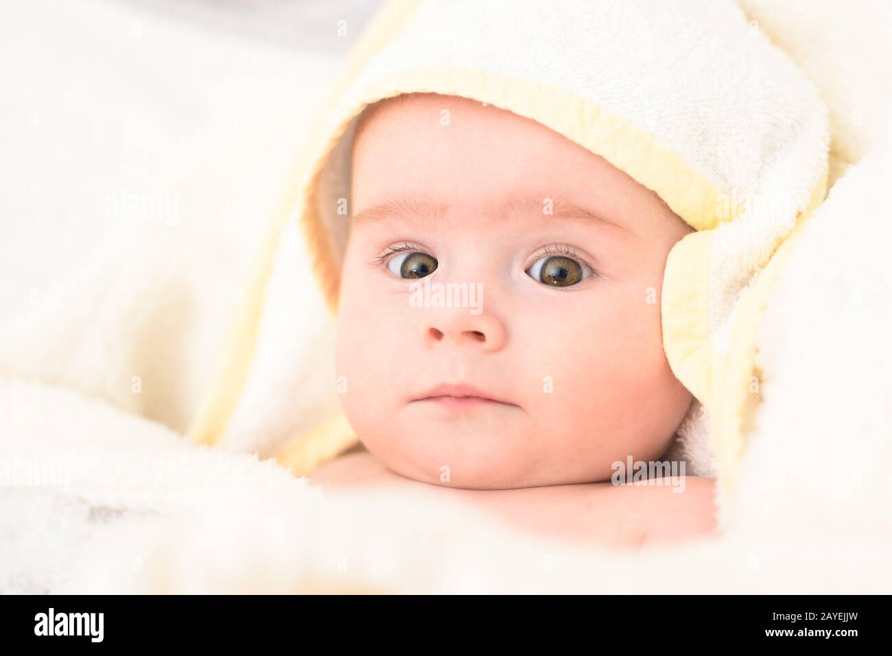 Adorable 6 Monate alten Baby Kleinkind auf ein Bett auf dem Bauch mit dem Kopf nach oben in die Kamera schaut mit ihren großen Augen. Natürliches Licht. Stockfoto