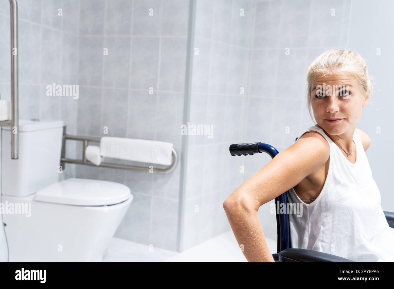 Blondes Mädchen sitzt im Rollstuhl in einem Badezimmer, hinter der toilette,  mit dem Kopf seitlich gedreht Stockfotografie - Alamy