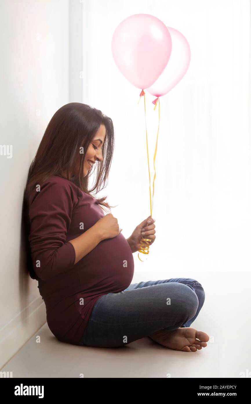 Schwangere Frau mit Luftballons in der Hand und lächelnd an ihrem Baby-Bump. Stockfoto