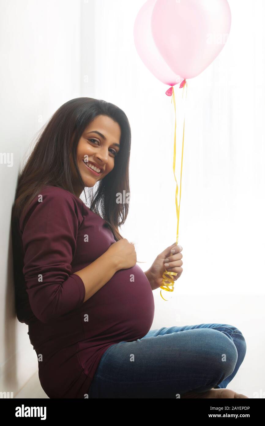 Schwangere Frau sitzt mit Luftballons in der Hand und lächelt. Stockfoto