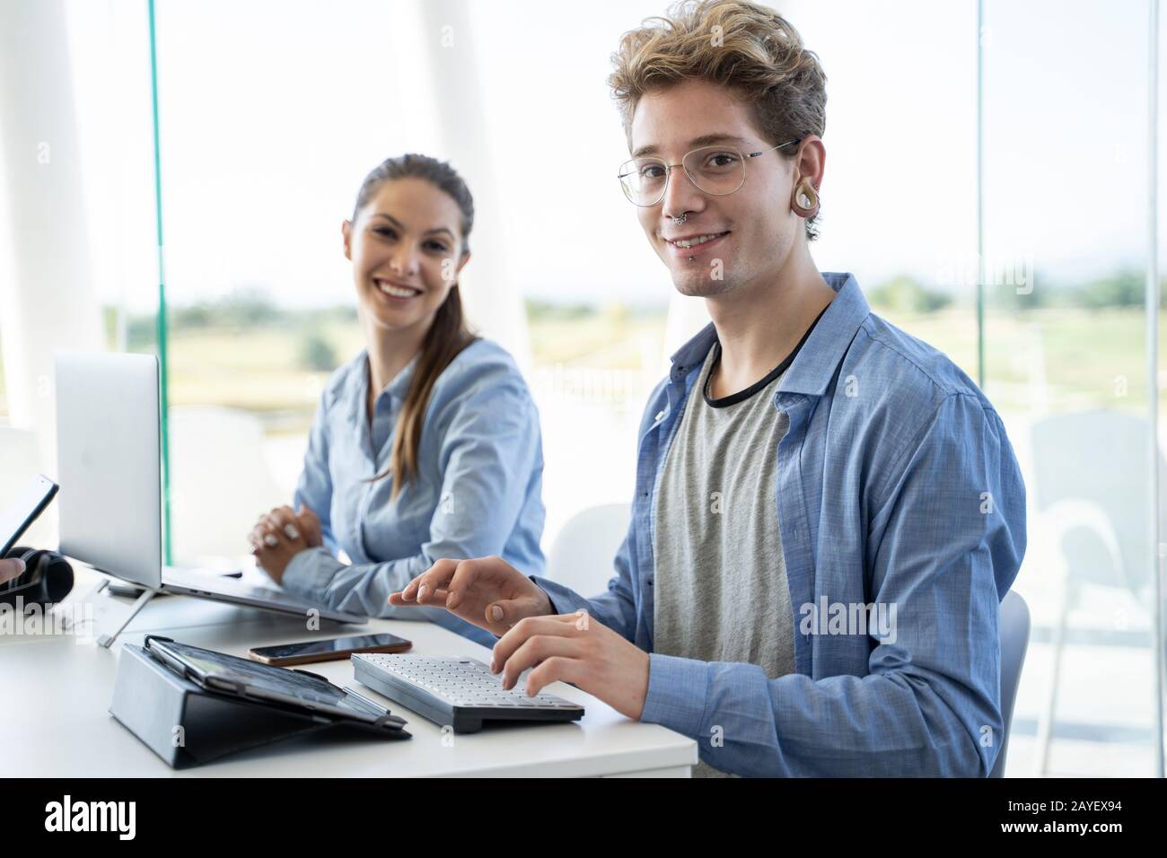Junge Paare betrachten die Kamera und arbeiten an ihrem Computer in einer Feigheit Stockfoto