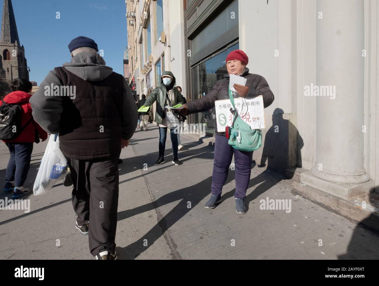 An einem kalten Tag verteilen chinesische Amerikanerinnen Werbeflieger in chinesischer Sprache an der Main Street vor der Roosevelt Ave. In Chinatown, Flushing, NYC Stockfoto