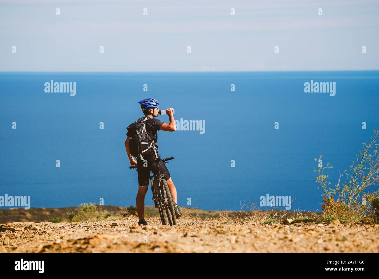 Ein junger Kerl auf dem Mountainbike gestoppt Wasser aus einem Krug auf ein steiniger Weg in der Nähe des Mittelmeers zu trinken in Spanien. Stockfoto