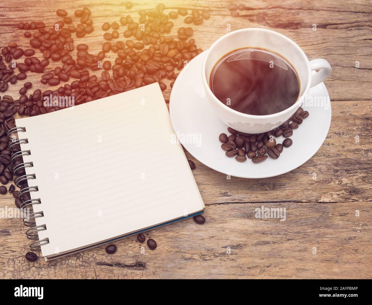 Heiße Kaffeetasse mit Kaffeebohne und Notizbuch auf Holztisch. Kaffee Hintergrundmenü für Café oder Café-Bar Stockfoto