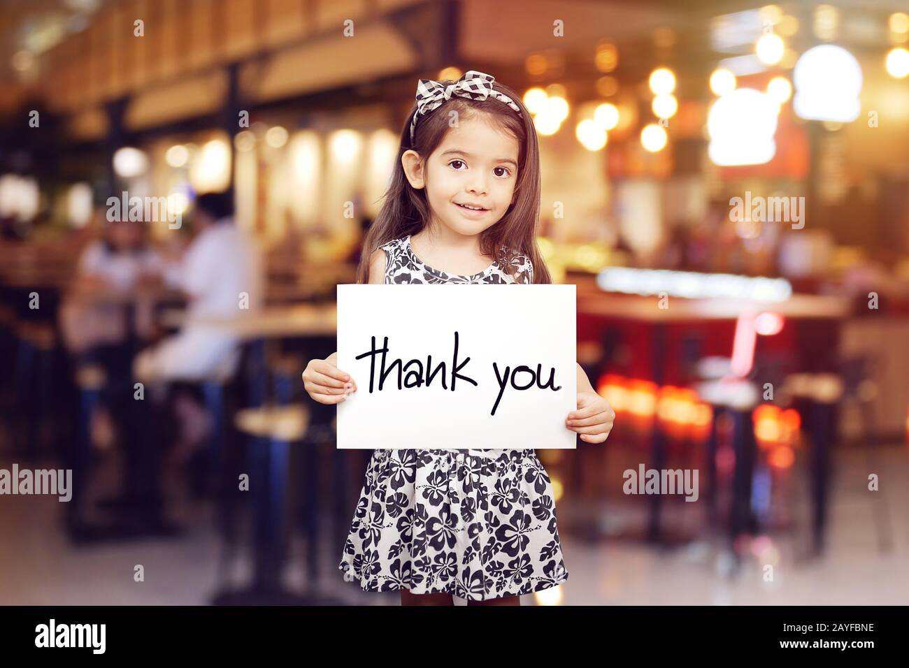 Süßes Mädchen, das ein Stück Papier mit den Worten "Danke" hält, verwischt den Restauranthintergrund Stockfoto
