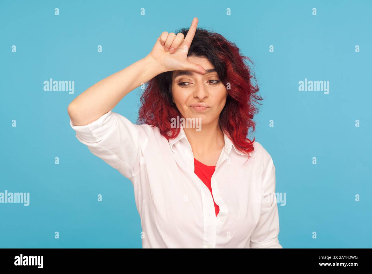 Ich bin Verlierer! Porträt einer unglücklich depressiven Hüftfrau mit ausgefallenen roten Haaren, die L-Zeichen auf der Stirn zeigt, die Verlierer-Geste macht und sich unsicher fühlt, disa Stockfoto