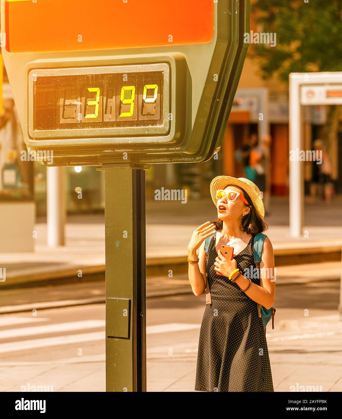 Frau leidet bei heißem Wetter im Freien unter Hitze und Sonneneinschlag vor dem Hintergrund eines Straßenthermometers mit 39 Grad Celsius Stockfoto