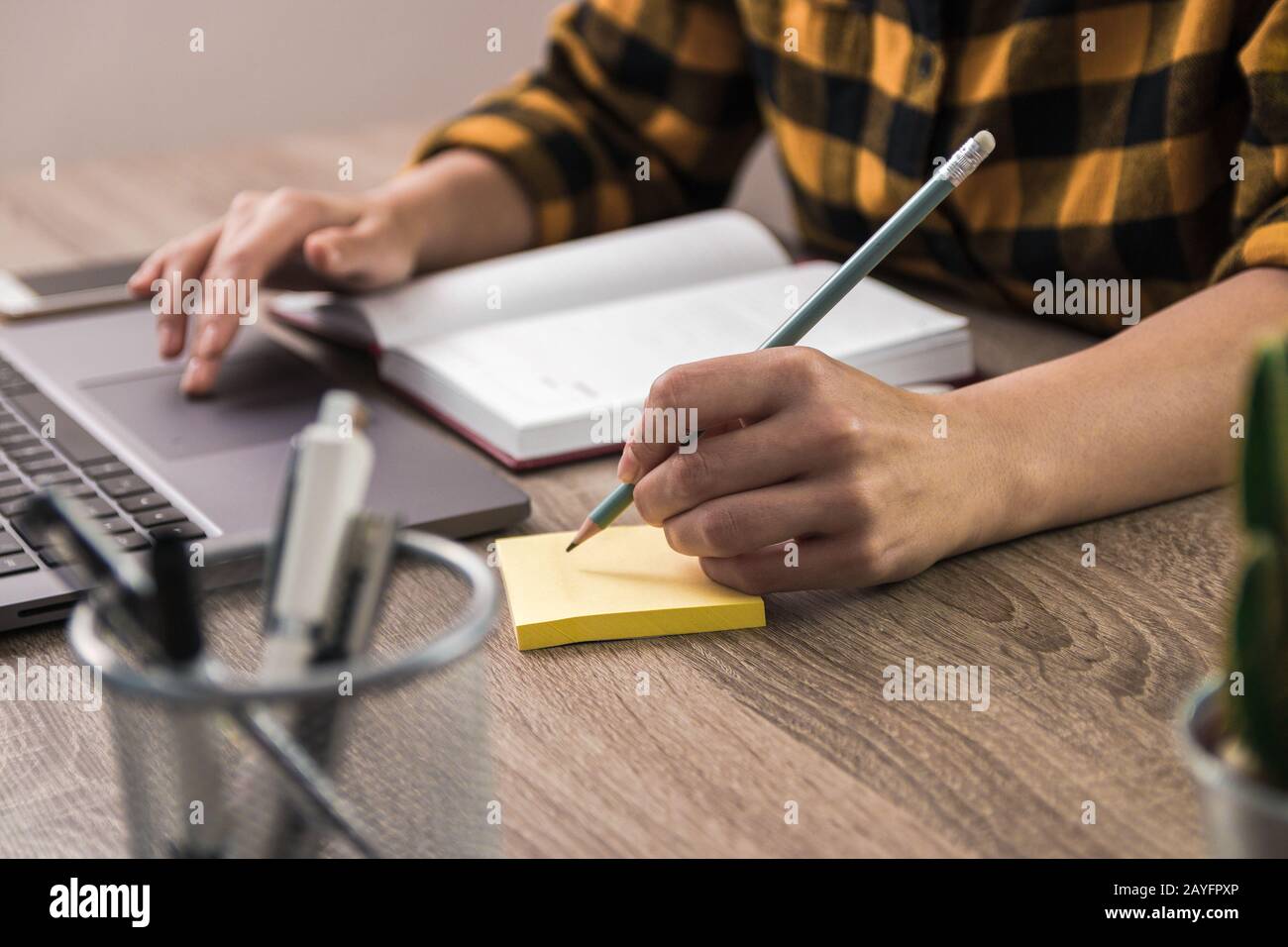 Kurze Notiz: Nahaufnahme der Hände einer Geschäftsfrau, eines Studenten oder eines Freiberuflers in einem gelben Hemd, die eine Notiz auf eine Haftnotiz macht Stockfoto