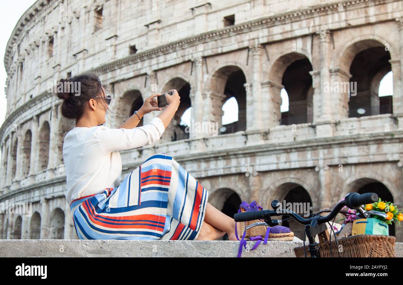 Schöne junge Frau Bilder aufnehmen mit Smartphone sitzen vor dem Kolosseum in Rom bei Sonnenuntergang. Stockfoto