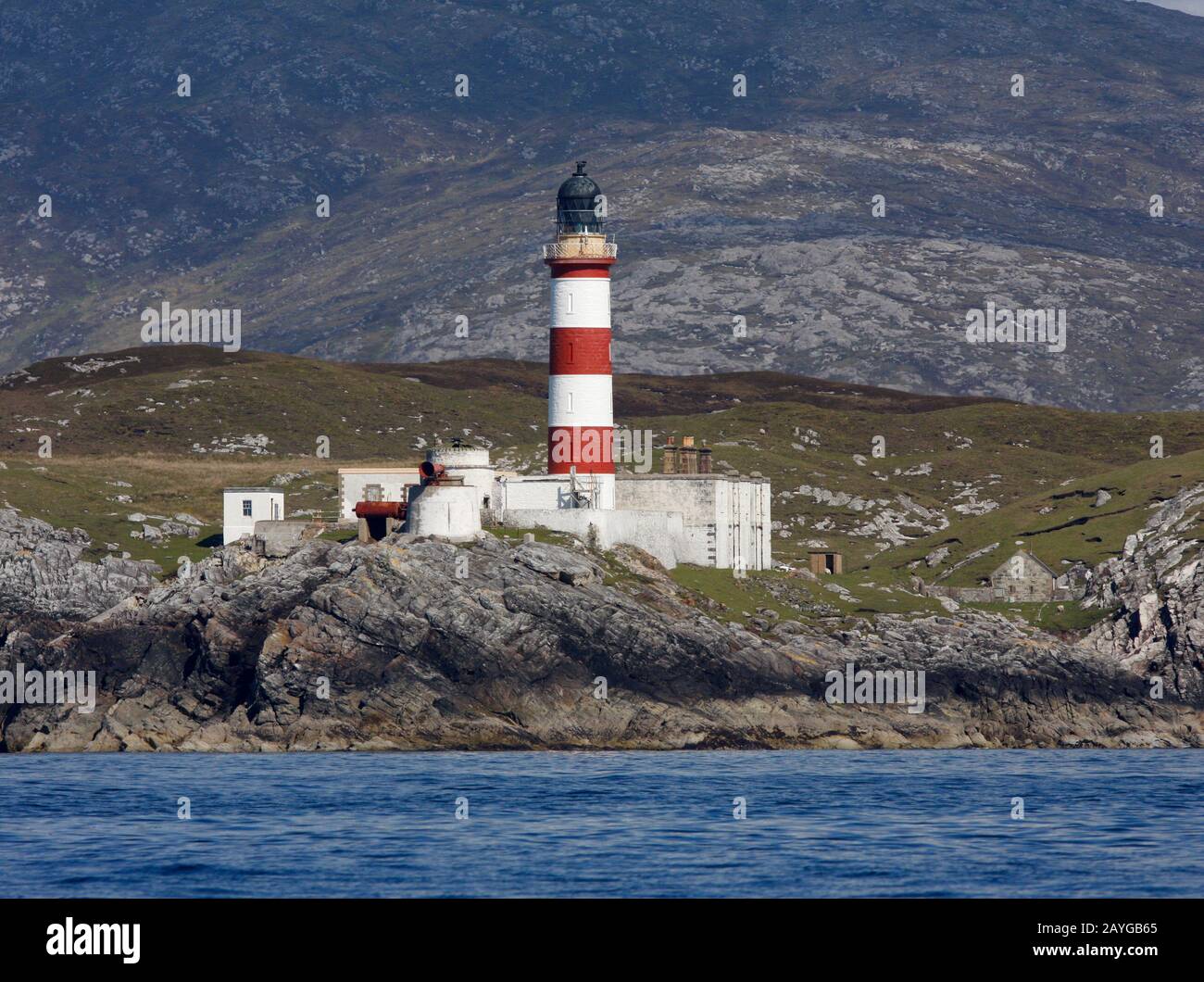 Der hohe, rot-weiß gestreifte Eilean-Glas-Leuchtturm, Scalpay, aus dem Meer, mit den Hügeln von Harris hinter, Western Isles, Schottland Stockfoto