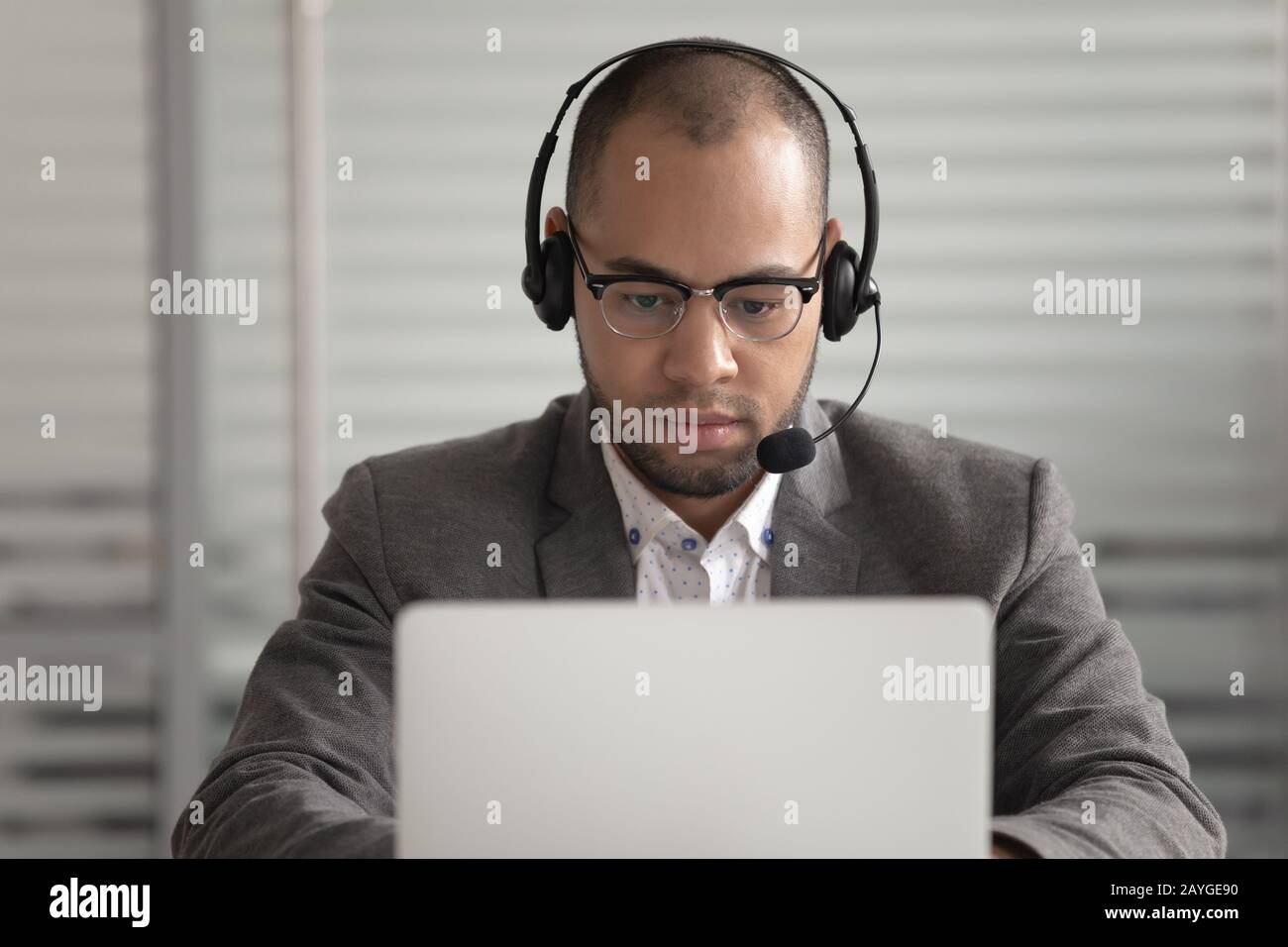 Konzentrierter männlicher Mitarbeiter im Headset, der mit der Arbeit am Laptop beschäftigt ist Stockfoto