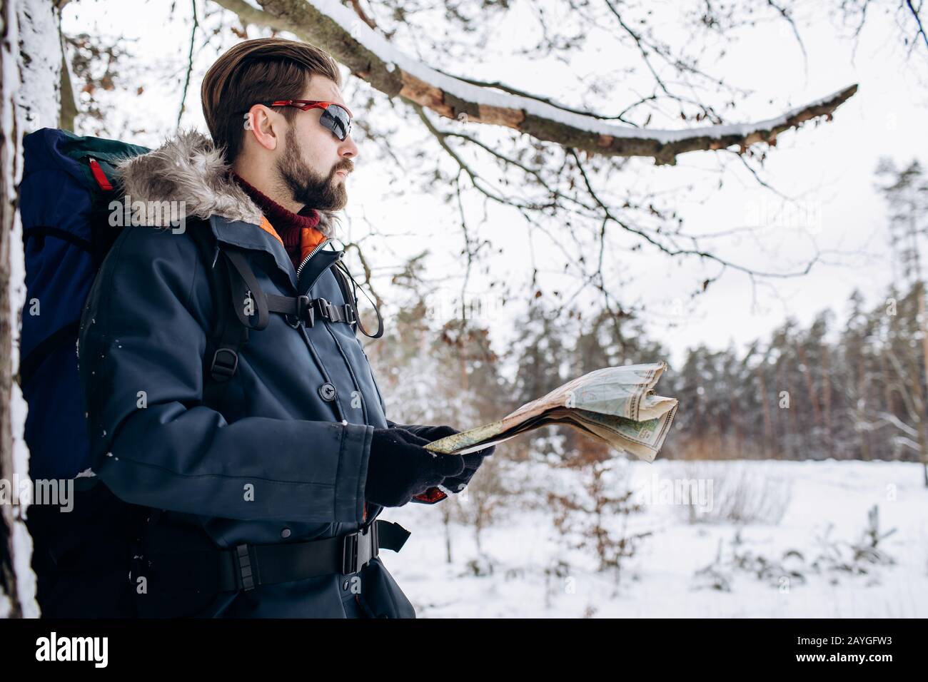 Seitenansicht von braunhaarigen bärtigen Touristen mit Karte und Rucksackwandern im Winterwald Stockfoto