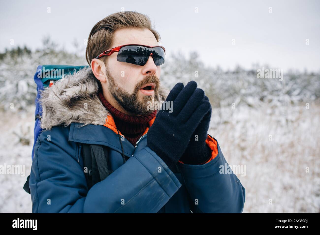 Braunhaariger stilvoller männlicher Tourist, der versucht, sich während der Winterreise warm zu machen Stockfoto